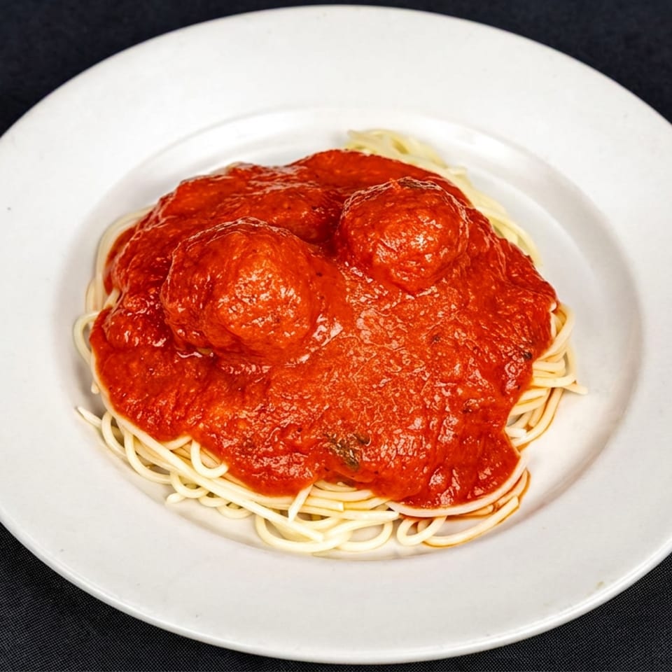 Spaghetti topped with three meatballs and rich tomato sauce on a white plate against a black tablecloth.