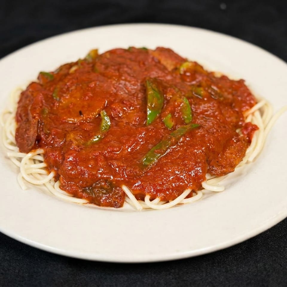 Plate of spaghetti topped with chunky tomato sauce, green peppers, and herbs on a white dish.